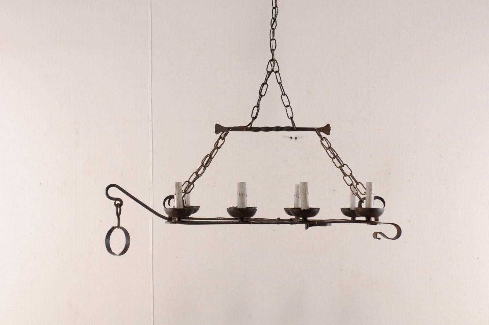 A French midcentury, eight-light forged-iron chandelier made from a 19th century spit-jack. A spit-jack is a type of rotisserie that was once common in fireplaces. This chandelier has eight arms, four along each outer side, which connect to the