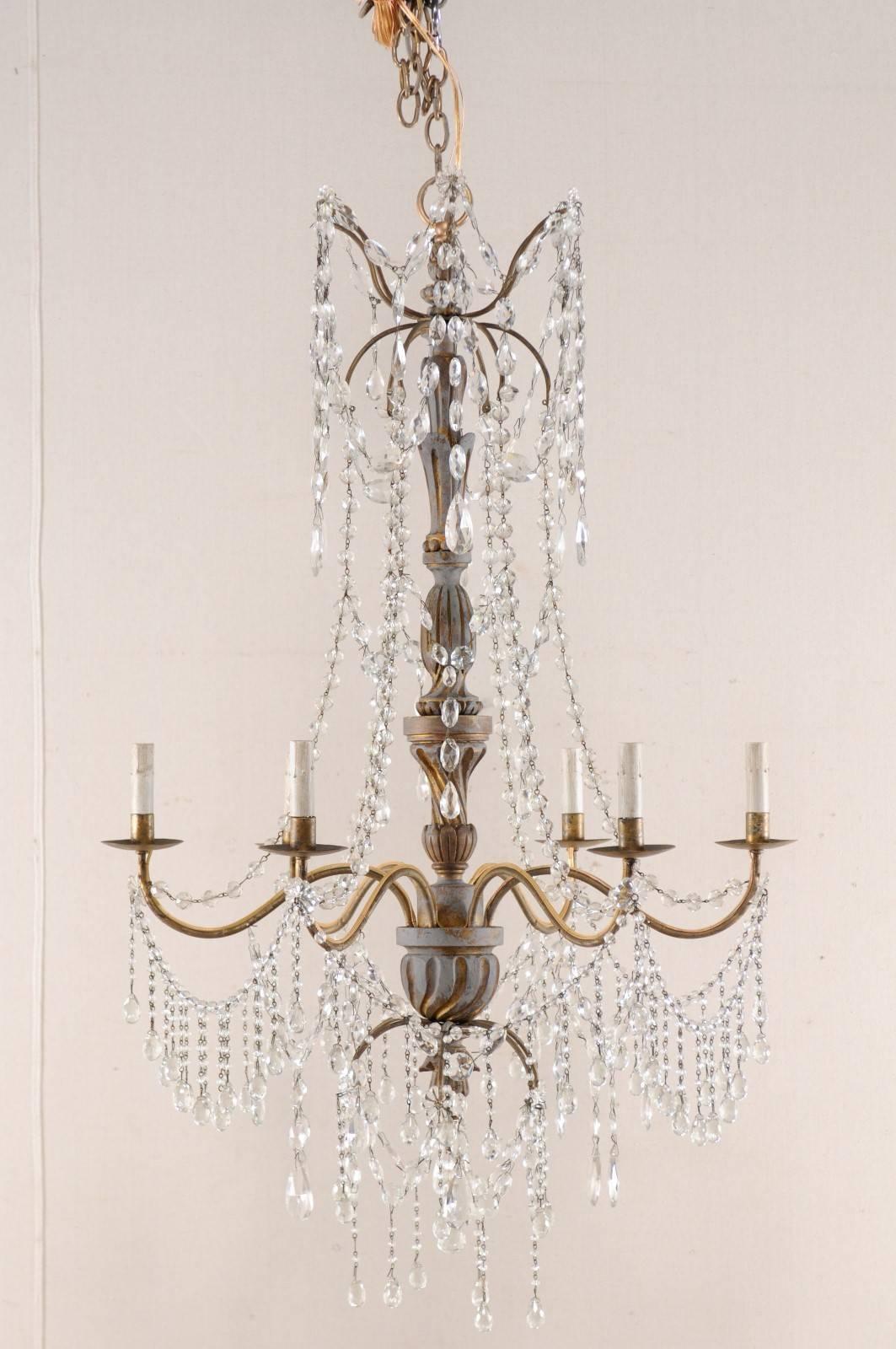 An antique Italian six-light crystal chandelier with gilt and painted wood central column. This Italian chandelier, from the early to mid-20th century, features an exquisitely carved wood central column with six metal S-shaped arms swooping outward,