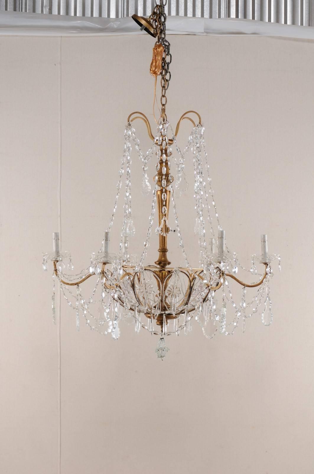 A vintage Italian crystal chandelier with carved wood central column. This Italian chandelier features a beautifully carved and gilded central column adorn with a display of crystals and Italian glass beaded swags splaying down from it's top,