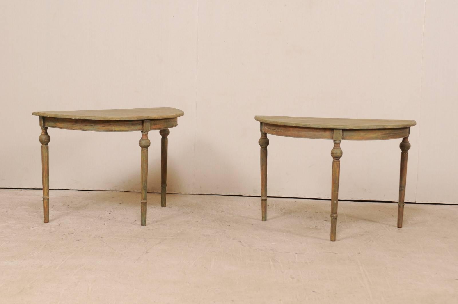 A pair of 19th century Swedish demilune tables. This pair of antique Swedish painted wood demilune tables features half moon tops over rounded aprons. The pair is raised on beautifully turned legs with a more bulbous accent near their tops. These