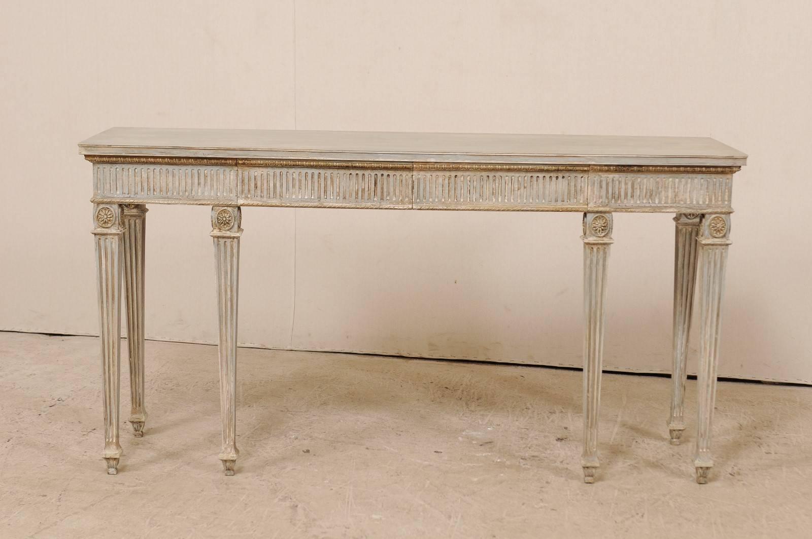 A Gustavian style carved wood console table. This vintage American console table has a beautiful Gustavian style and features fluting details about the apron and legs, roped trim molding, and carved floral medallions around each knee. The table is