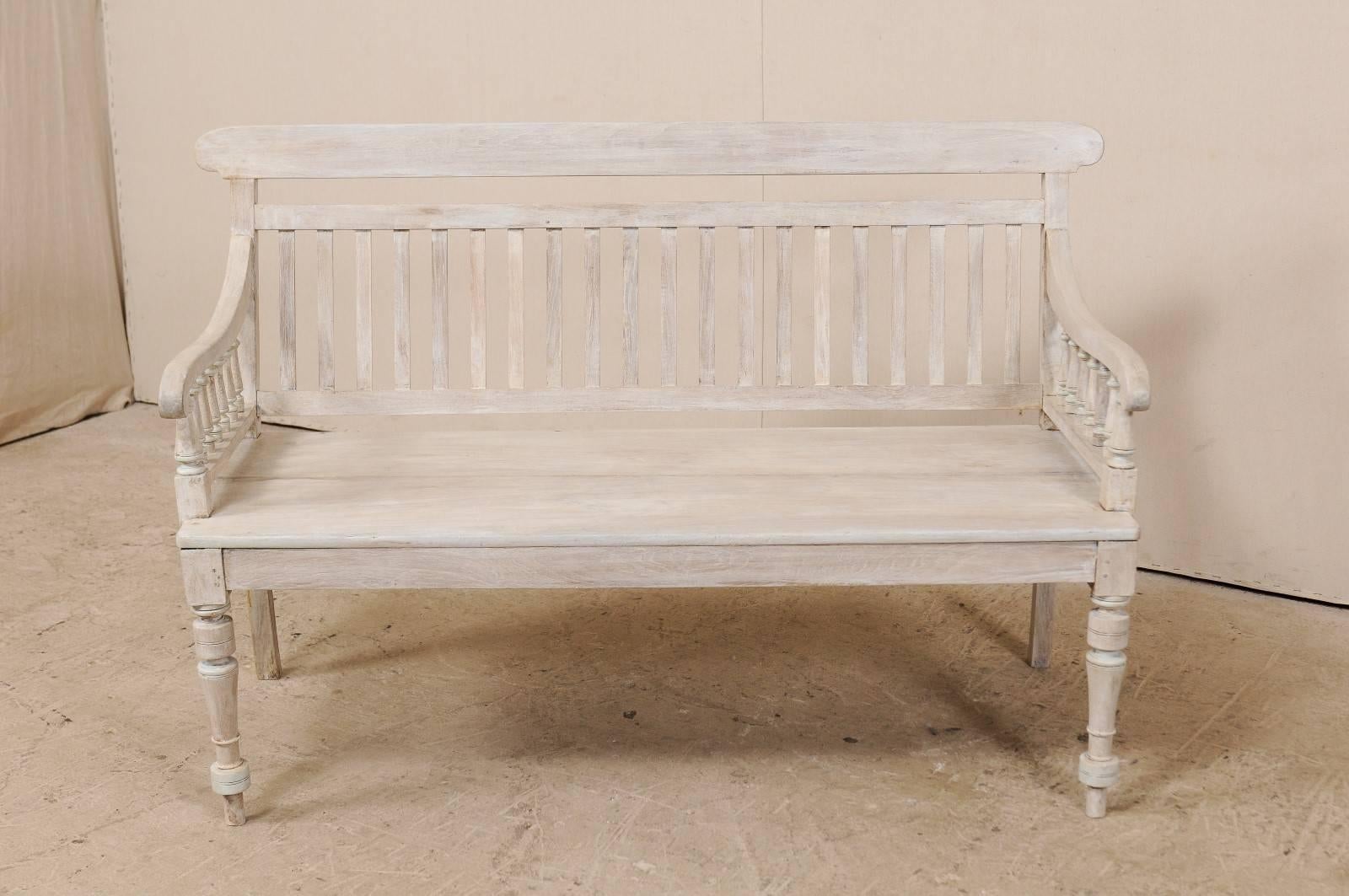 A British Colonial painted teak wood bench. This British Colonial style teak wood bench is from the mid-20th century, India. This sofa bench features turned front legs, a vertical slat back, banister style arms and curled knuckles. Teak is a