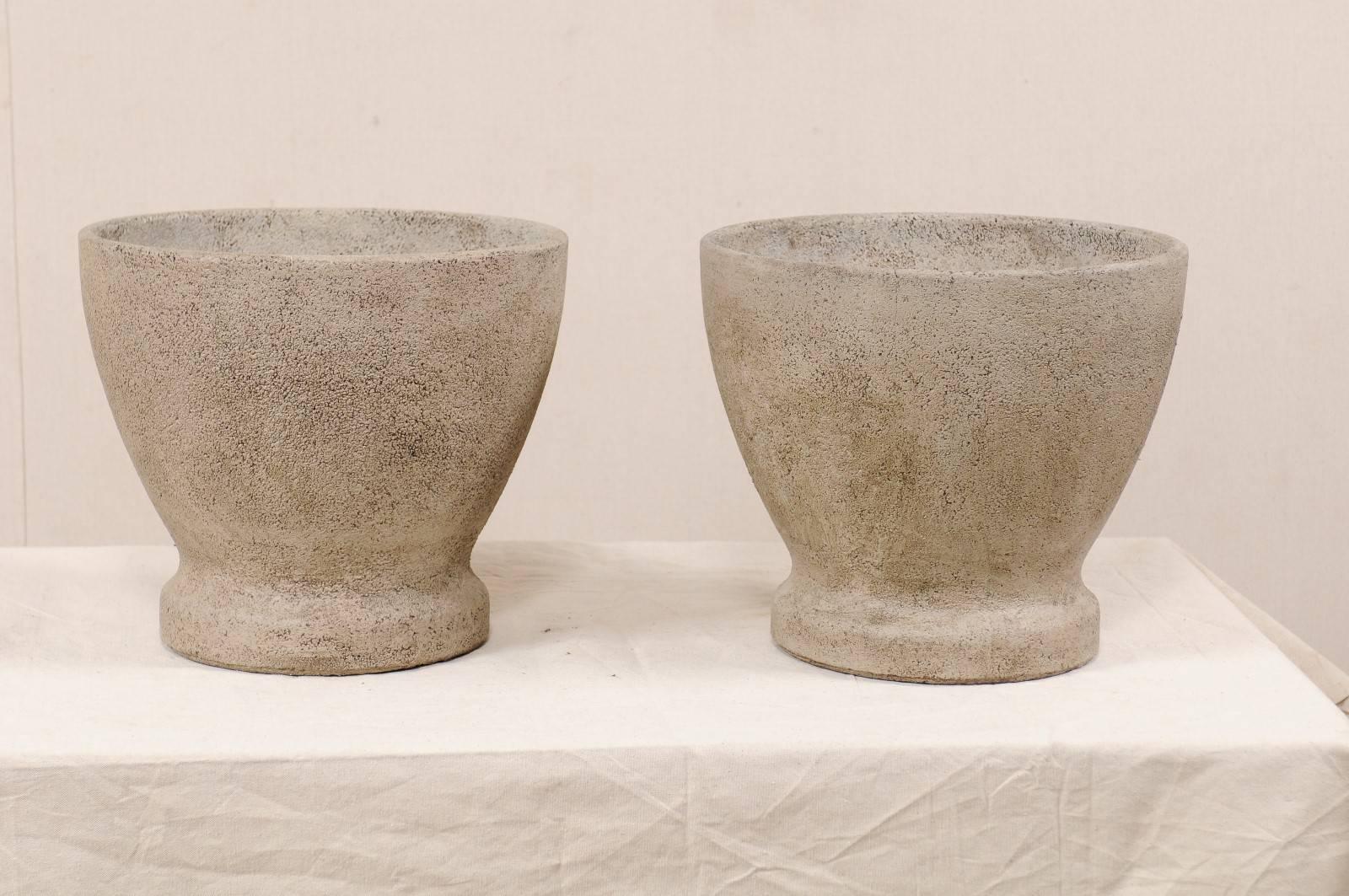 A pair of French cast stone planters from the mid-20th century. This pair of vintage French planters have been made of cast stone and have a simple, clean design element to them. These round-shaped planters are wider at their tops lips and gently
