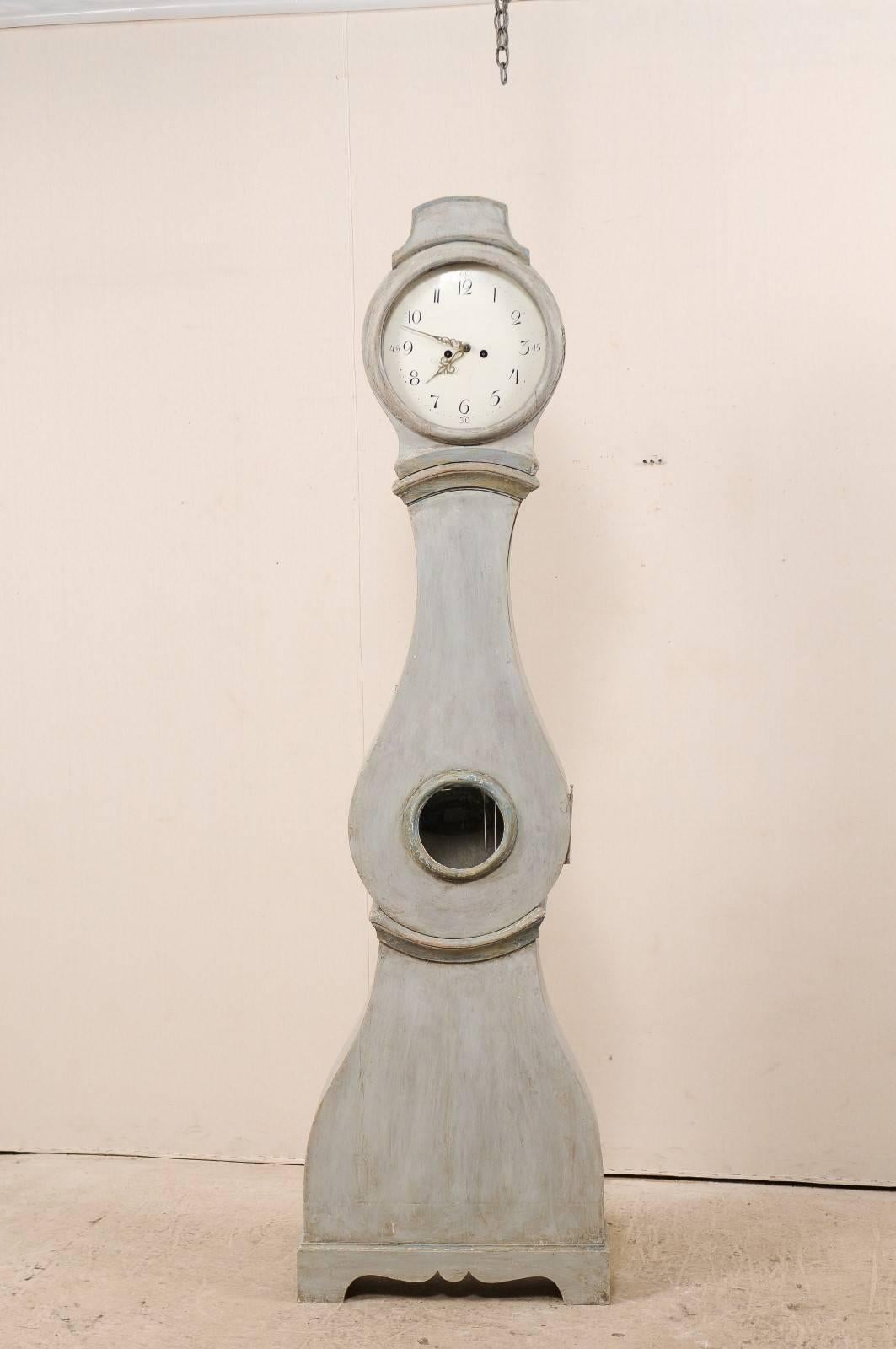 A 19th century Swedish grandfather clock. This Swedish clock features a round face, subtly raised bonnet, and raindrop shaped body. The head of this clock has a glass window at its right side, allowing one to see the mechanics of the clock at work.