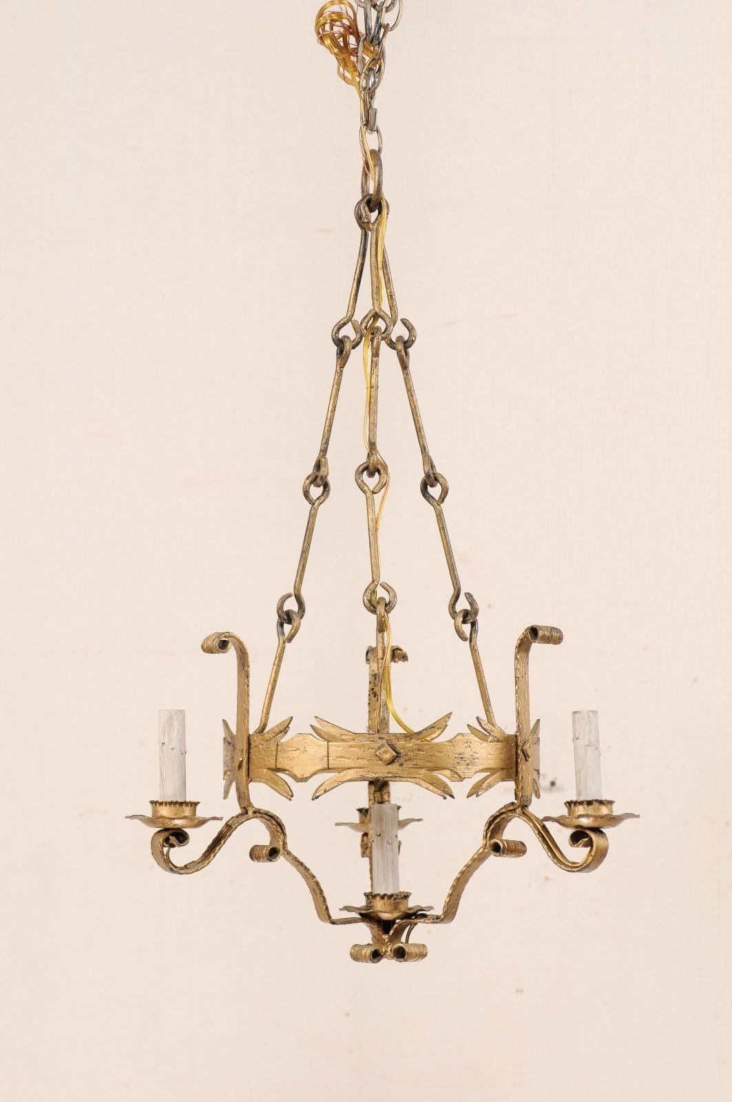 A French four-light gold painted iron chandelier from the mid-20th century. This vintage French chandelier features an ornately decorated cut-iron central ring with three lights mounted about it's perimeter, and a lower single light centered within