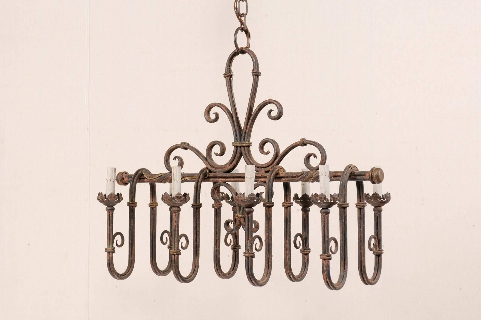 A vintage French eight-light iron chandelier. This French chandelier from the mid-20th century features an overall rectangular shape which is made up of a horizontally positioned metal center beam with twists and has deeply swagged iron arms which