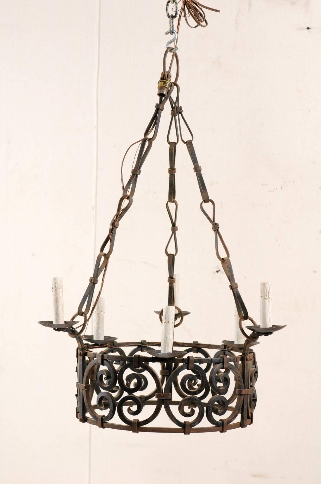 A French vintage six-light iron chandelier in a round ring shape. This French chandelier from the mid-20th century features an intricately designed centre comprised of c-scroll motifs about its ring. There are six short arms that lift slightly above