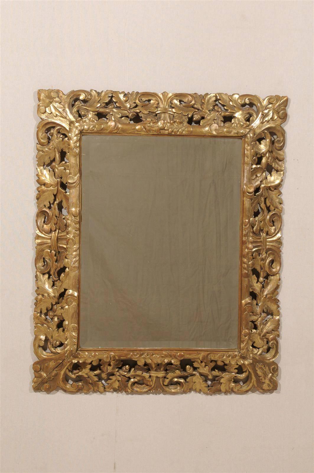 A French 19th century gilded mirror with beveled glass and floral motifs in the surround, including oak leaves, acorns and central motifs somewhat reminiscent of a stylized fleur-de-lys.