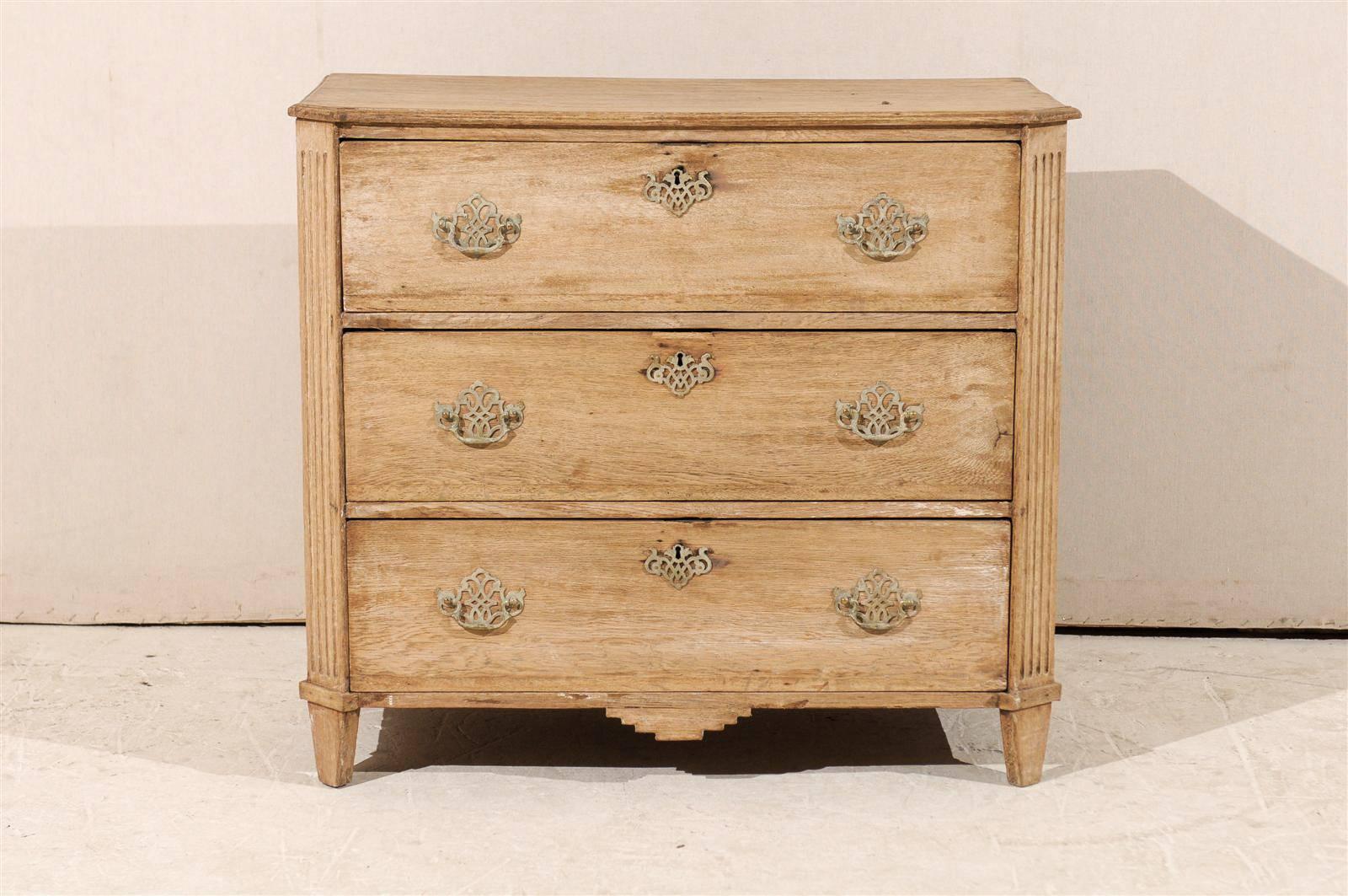 A 19th century English bleached three-drawer chest. This small size bleached English chest features three drawers with bail handles. The chest has beveled and fluted side posts above short angled and tapered feet. The skirt is nicely carved. With