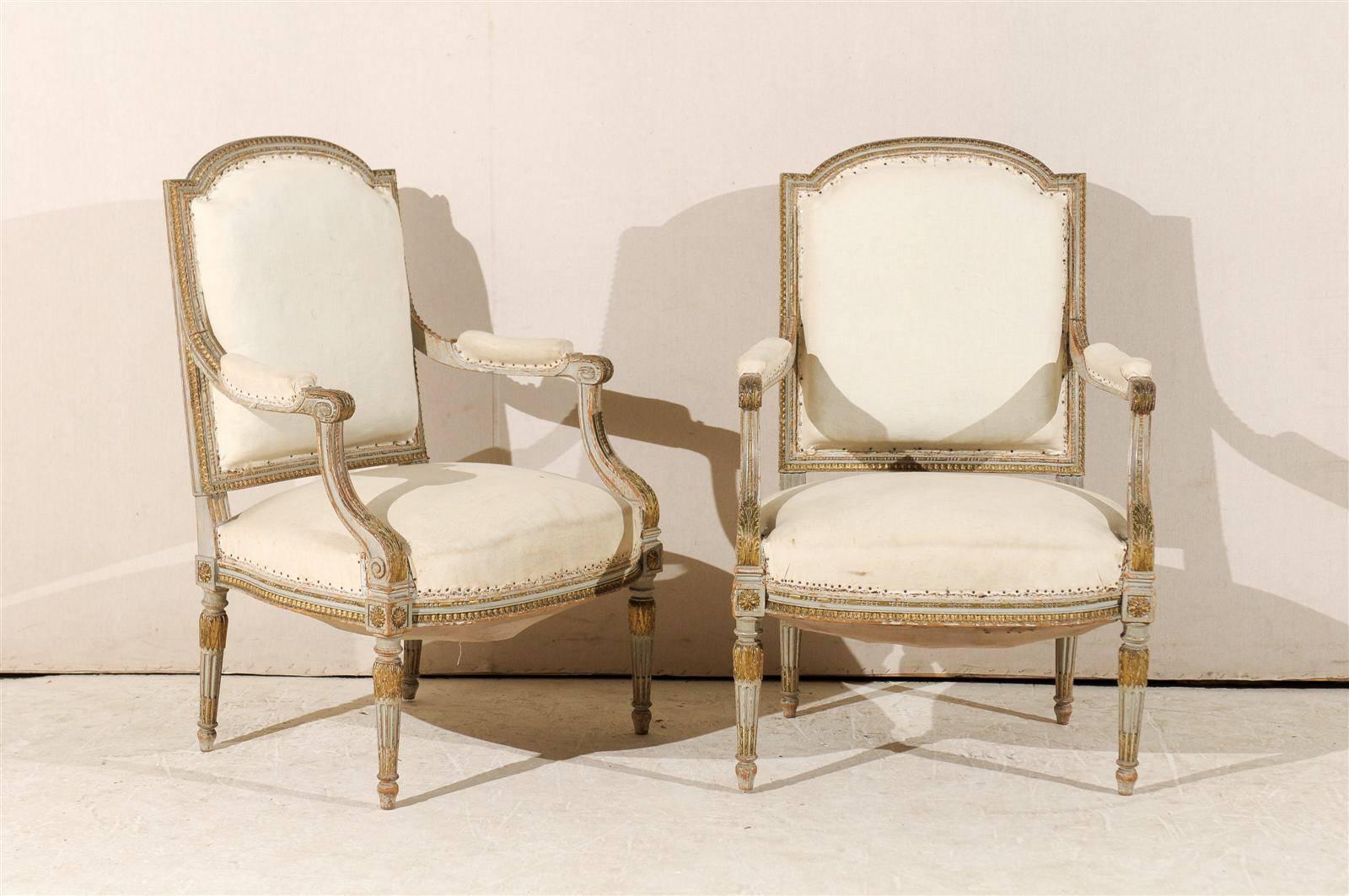 A pair of elegant French 19th century Louis XVI style fauteuils or armchairs with original paint, scrolled arms, fluted and tapered legs, gilded accents and Rosettes on the knees. Ready to be reupholstered. This pair would add a touch of beauty to
