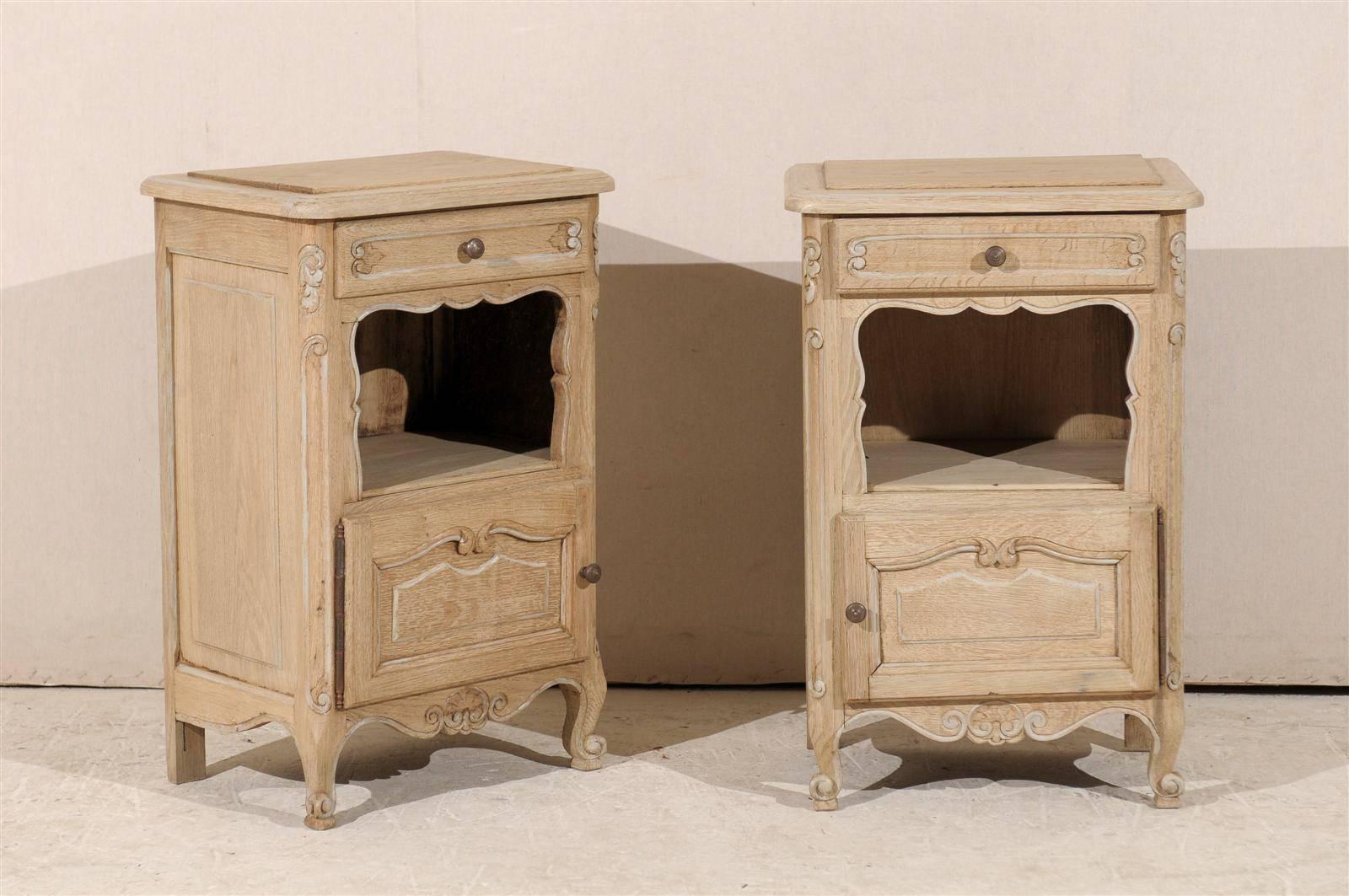 A pair of French early 20th century wooden chests with single drawer, open shelf section and single door. Unfinished, with painted accents. Lovely carved apron, raised top and scrolled feet.
 