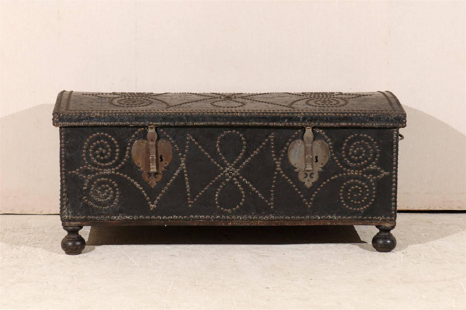 A Spanish 19th century trunk made of leather embossed with brass nailheads featuring geometrical patterns and heart shapes on the sides surrounding the handles. Bun feet.