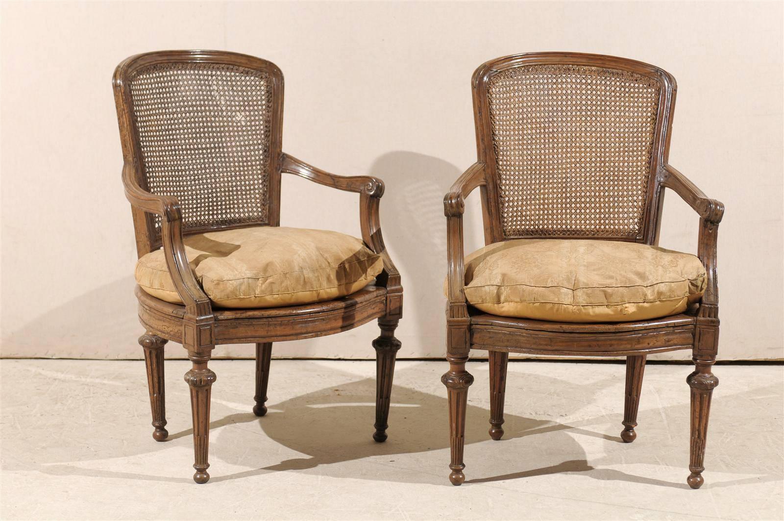 A pair of 18th century Italian wooden armchairs with cane seats and backs, tapered legs, scrolled arms and cushions.