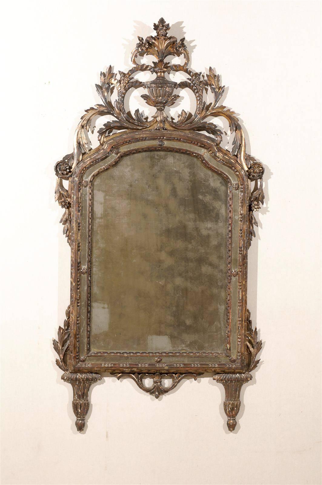 An Italian 19th century wooden mirror with traces of gilding and beautifully carved crest featuring an urn and flowers. Beyond the first wooden molding around the central mirror, panels of glass form another layer in the frame.

  