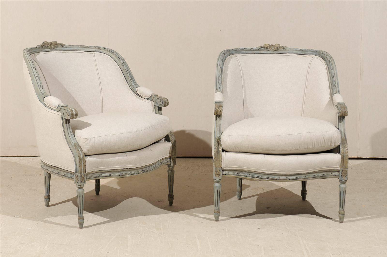 A pair of French Louis XVI style painted wood barrelback armchairs Reupholstered in Belgian linen with discreet gilt accents, scrolled and upholstered arms, fluted legs with rosettes on the knees, acanthus leaves and rose carvings on the top. Two