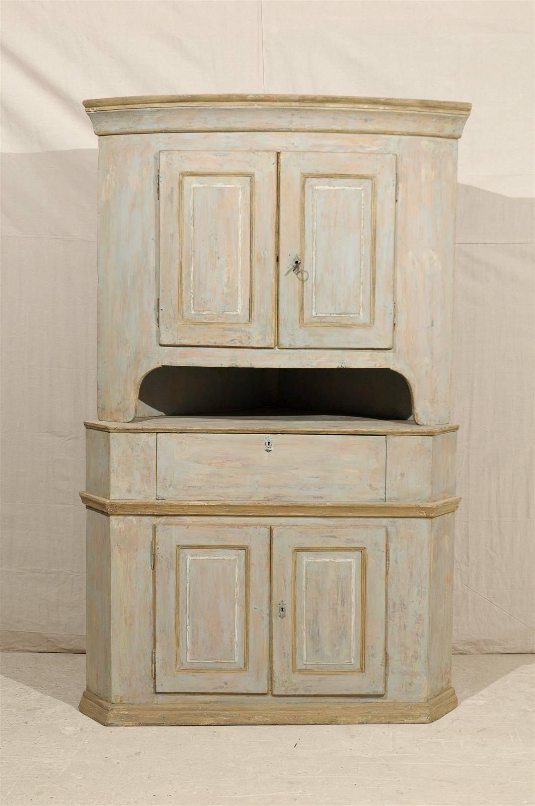 A large Swedish early 19th century Karl Johan corner cabinet made of painted firewood with raised panel doors, convex upper body, multiple inner shelves opening in the center and angled sides. The Karl Johan is the period that follows the Gustavian