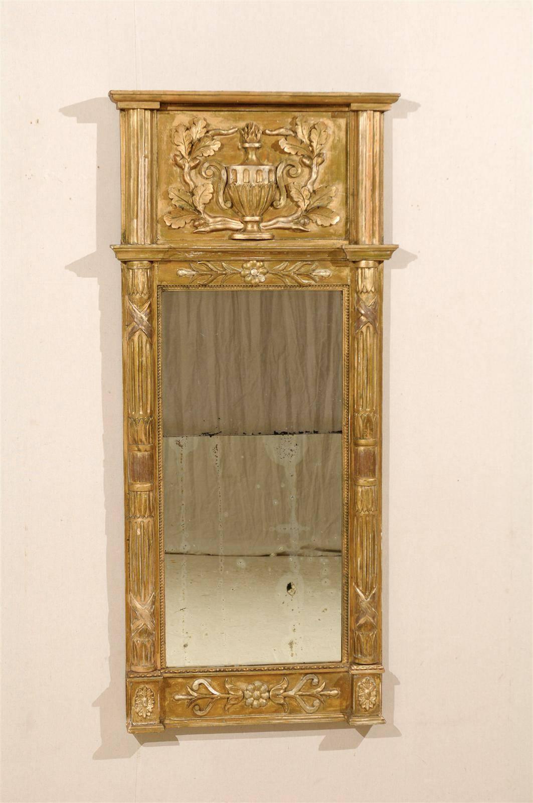An exquisite Swedish 19th century gilded wood slender mirror with carved fire urn and floral decoration and sides flanked with fluted half-columns. Gilt over gesso.