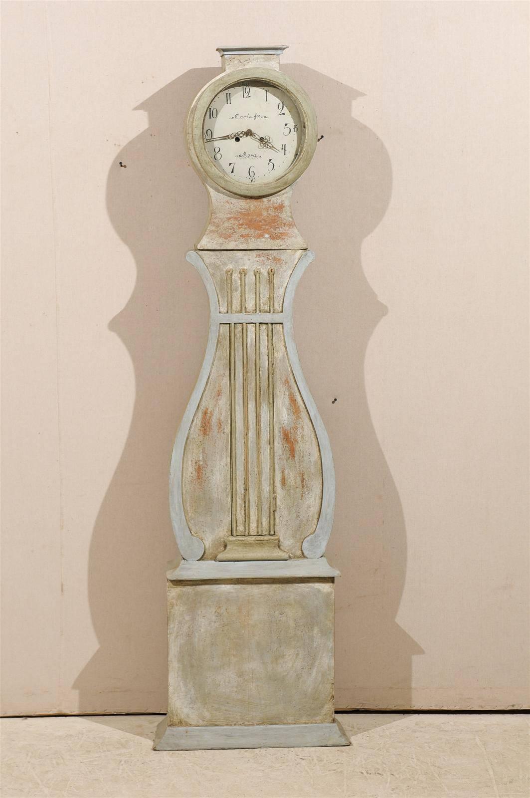 A Swedish 19th century painted wood clock (Commonly Called a Mora Clock) with lyre shaped door and flat carved crest. This clock retains it's original metal face, hands and movement.  This Swedish Clock has a flat carved top above its head and a