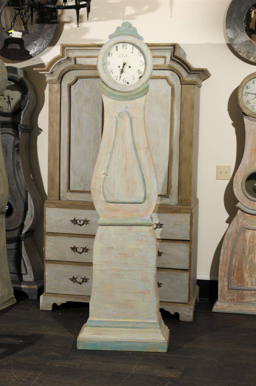 A Swedish 19th century painted wood Mora clock.  This Swedish clock is made of various tones, such as light grey with some wood coming through and green accents in the trim and crest.  The Mora clock stands out with the simplicity of its lines and