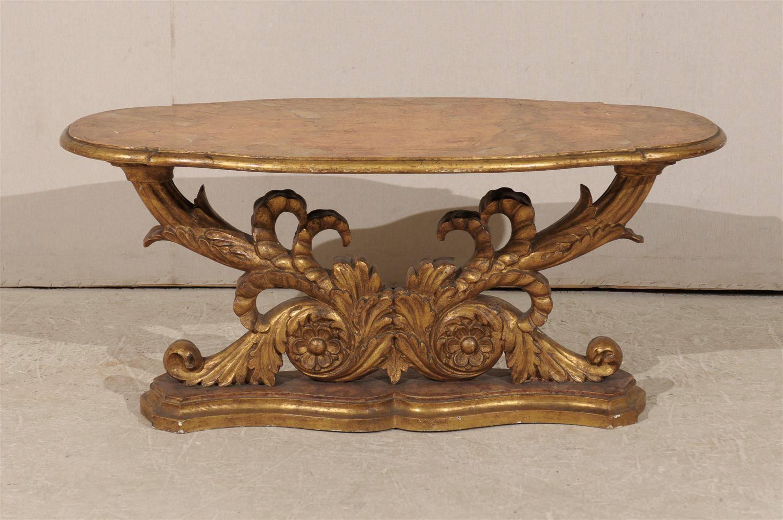 A Mid-19th century Italian gilded wood coffee table.  This Italian coffee table features a gilded base made of richly carved volutes supporting the oval faux marble top which sits on a faux-marble stand. The table has its original finish from the