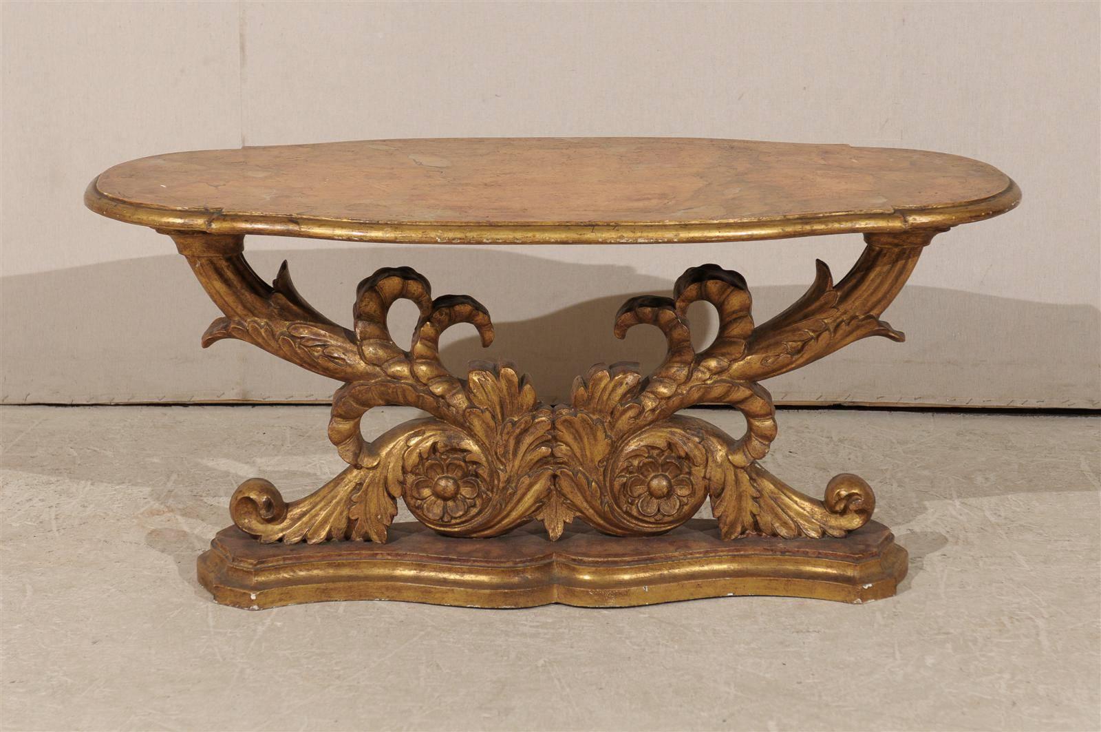 Tavolino in legno dorato italiano della metà del XIX secolo.  Questo tavolino italiano presenta una base dorata composta da volute riccamente intagliate che sorreggono il piano ovale in finto marmo che poggia su un supporto in finto marmo. Il tavolo
