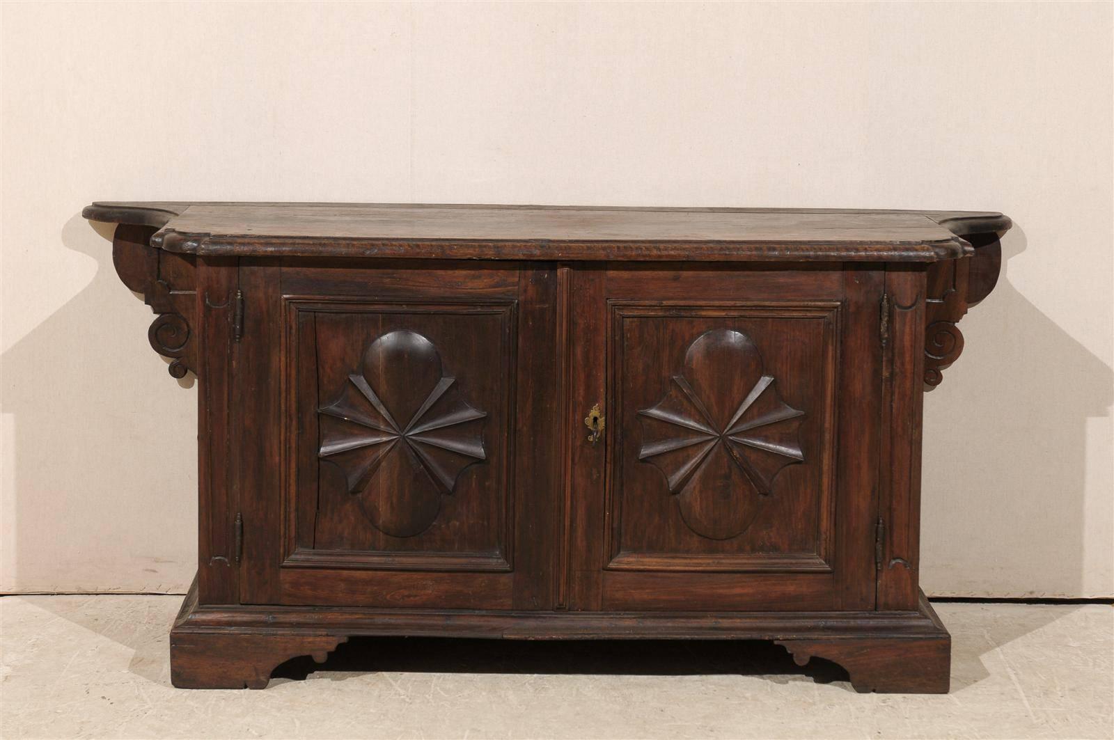 An exquisite 18th century Italian credenza / sideboard of deep brown colored walnut.  This piece features carved patterns including sun-rays on either door and either side panel.  The back of the credenza ends in a beautiful set of volutes and the
