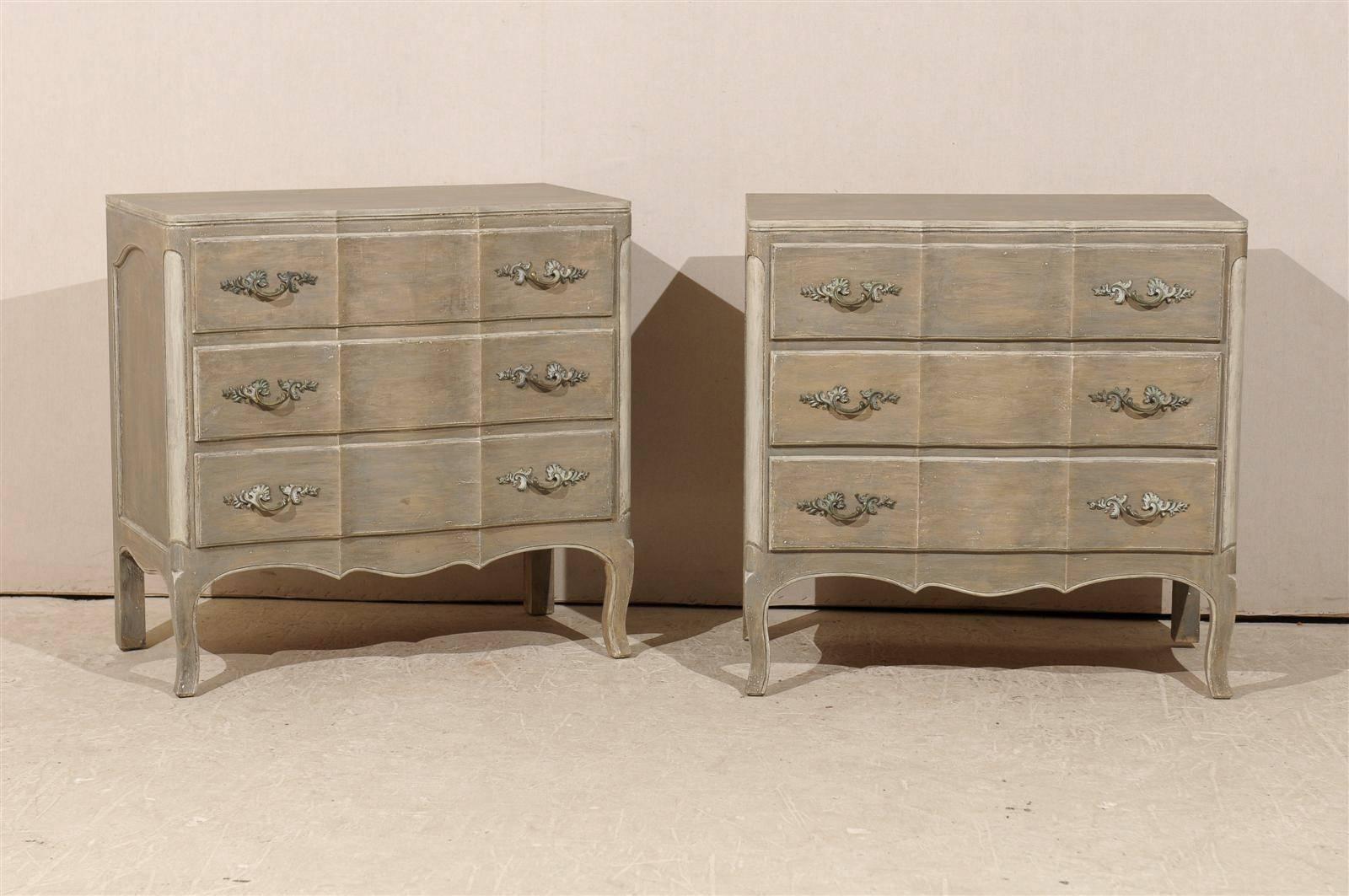 A pair of three-drawer serpentine front chests from Canada.

This pair of chests from the mid-20th century features a light grey green color with lighter accents on the carved side posts and a slightly serpentine front giving a nice discreet