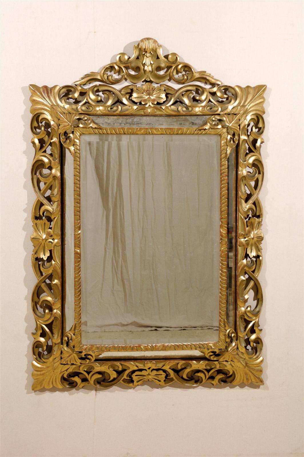An exquisite Italian carved and gilded mirror from the 19th century. This ornate mirror features an intricately carved crest and a decor of rinceaux (foliage) in its frame. This mirror is a nice warm gold tone, with some deep red undertones