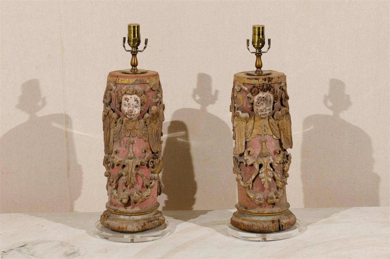 A pair of 18th century Portuguese painted red wood column table lamps with traces of gilding throughout.  These Southern European table lamps feature a wrap-around depiction that includes: carved angels, ornate scroll motifs and nicely carved