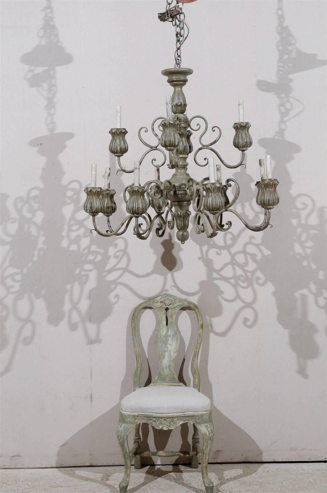 An Italian twelve-light painted wood chandelier of grey green color with central carved wood column. The arms are organized on two levels and made of s-scroll Motifs. The bobèches are shaped like exquisite tulip flowers. 20th century. This Italian