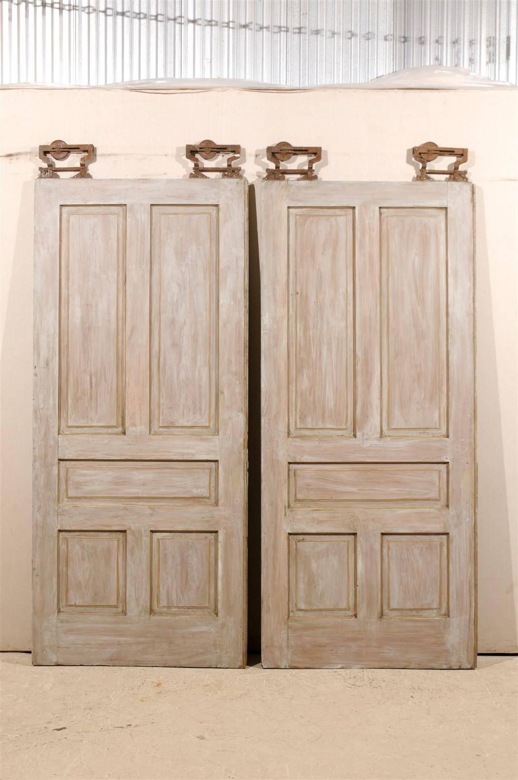 A pair of early 20th century American pocket doors with their original hanging hardware. This pair of early 20th century painted wood doors features a decor of carved motifs. Perfect space savers, their pastel light grey color would blend nicely