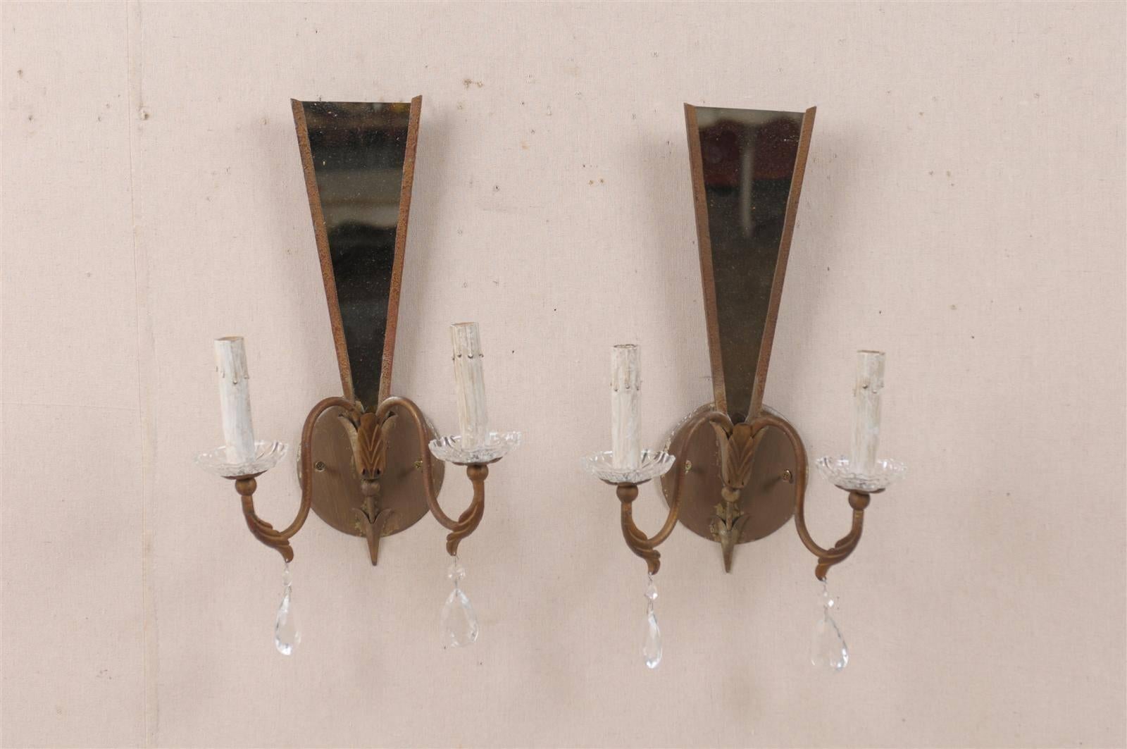 A pair of vintage modern French mirror backed sconces with crystal accents. This pair of mid-20th century French sconces features a triangular mirrored backplate supporting two swoop arms. Two delicate crystals and acanthus leaf motifs decorate the