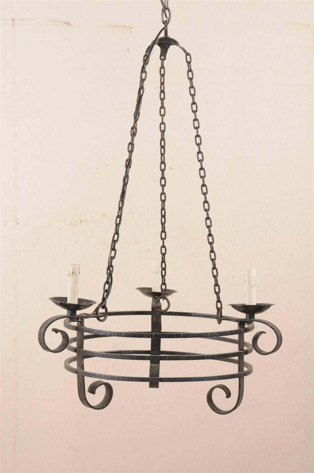 A French vintage forged iron three-light chandelier. This unusually shaped mid-20th century forged iron chandelier features a circular central part made of three rings, supporting three scrolled arms. Three chains are hooked up together at the