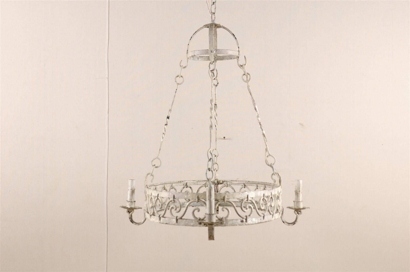 A French vintage oval chandelier. This French mid-20th century four-light chandelier features a central ring decorated with a running motif of volutes. The scrolled arms support the small bobèches and painted candle sleeves. This French chandelier