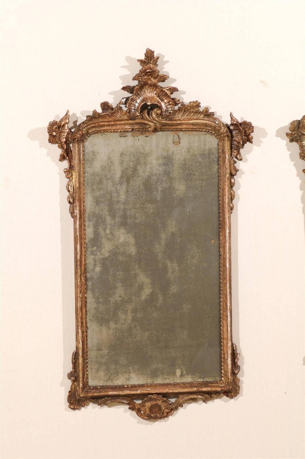 A pair of 18th century elegant Italian mirrors. This pair of Italian wooden Rococo style mirrors features nicely carved crests with floral and acanthus leaf motifs. The mirrors have their original hand-silvered glass. The frame has beaded motifs on