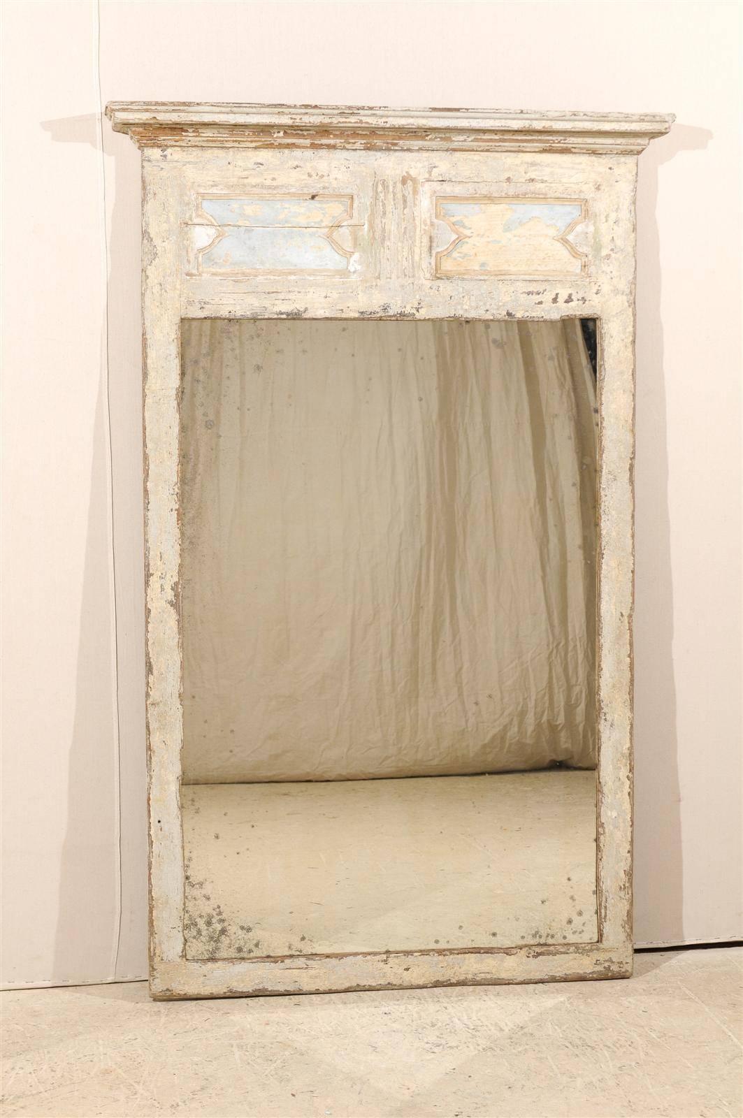 A large 19th century Spanish Trumeau mirror. This cream color Spanish painted and carved wood Trumeau mirror features two very faint blue motifs outlined with the slightest red tone sitting under the cornice. The glass is old and has antiquing