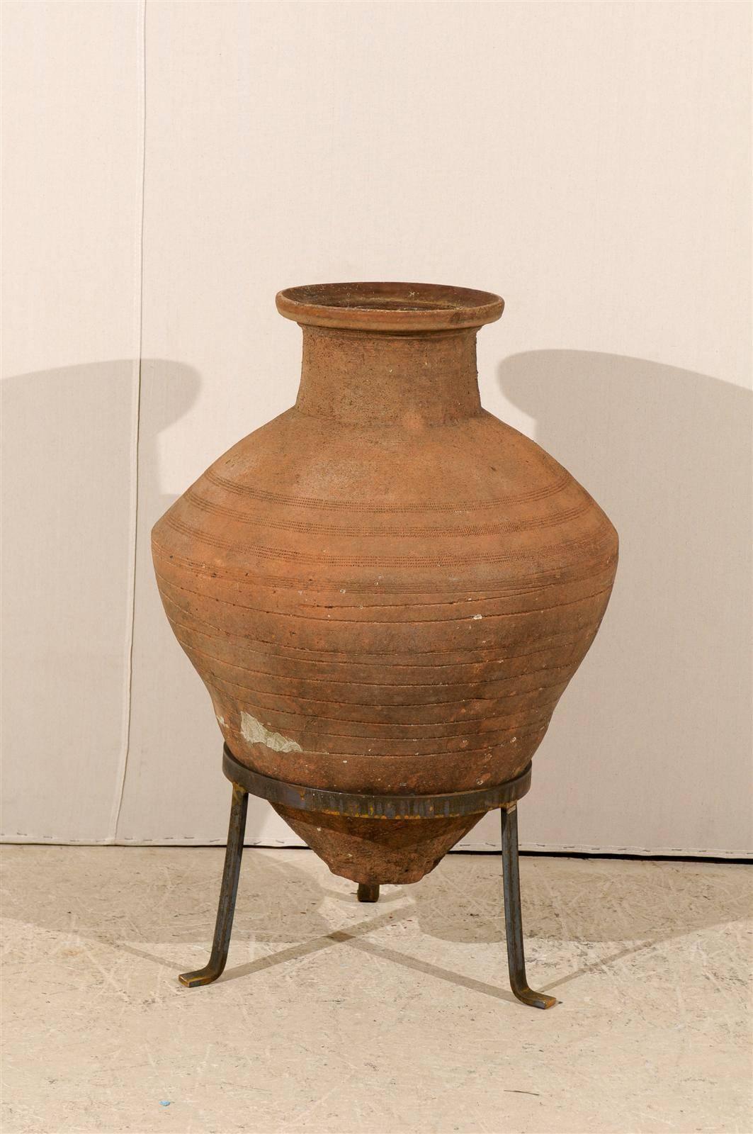 A European olive jar from the mid-19th century. This terracotta olive jar features a beautiful coloration and shape. The jar is raised on a custom-made metal tripod base. The dimensions mentioned below are with the stand.