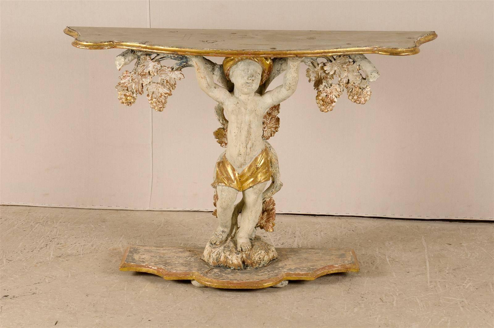 An exquisite early 18th century Italian console table. This Italian console table features a painted and gilded wooden top supported by the carving of a putto. His loincloth and turban are gilded. He is backed by a grapevine carving. This piece