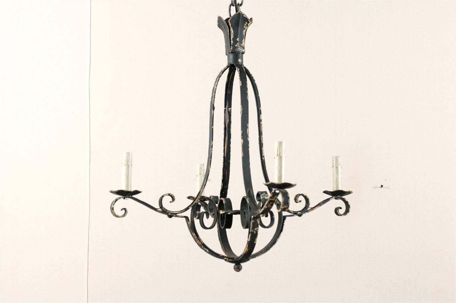 A French four-light chandelier. This French vintage mid-20th century light fixture has its nicely aged black paint with plaster over iron original finish. This chandelier features an elegant pear shaped central column with four scrolled arms flowing