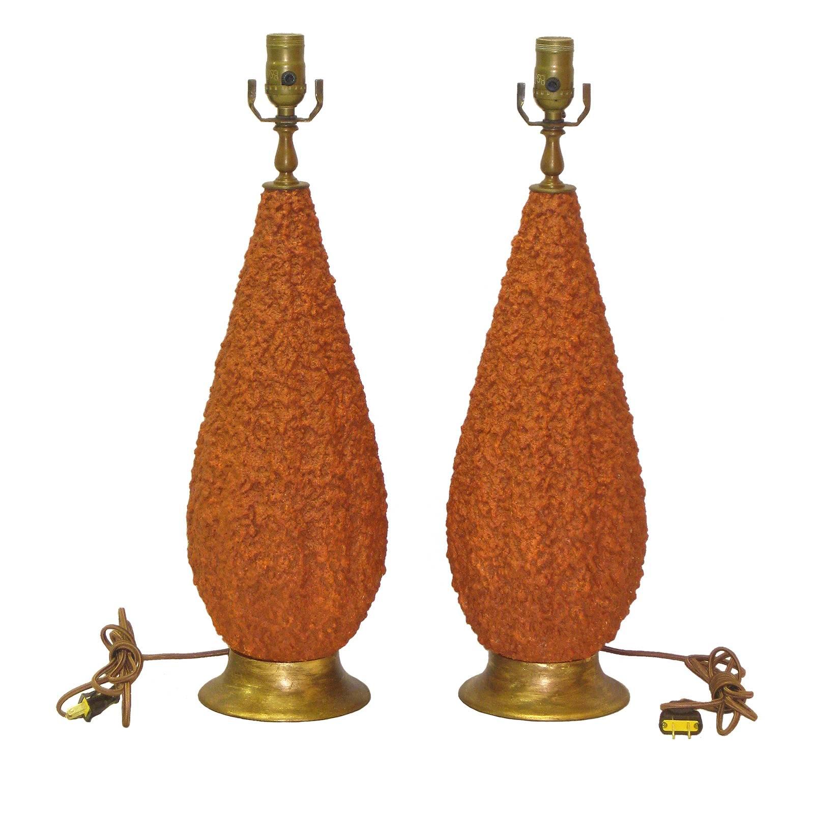 A pair of Mid-Century Modern teardrop-shaped coral ceramic lamps with stippled surface. This pair of American ceramic table lamps is raised on a dirty gold wooden base. The lamps are wired for the US market. The height provided below is to the top