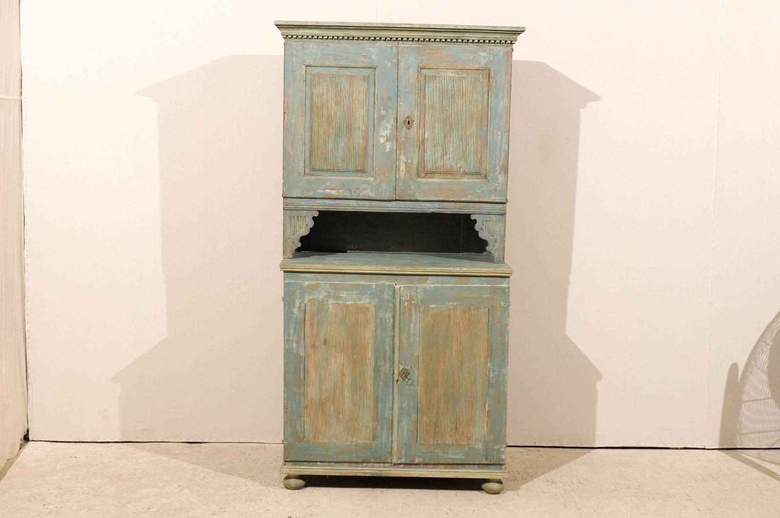 An 18th century Swedish late Gustavian cabinet with original paint. This painted wood cabinet features two reeded doors topped with a dentil molding. A pair of brackets/ volutes connect the top part to the lower doors, also reeded. The doors open up