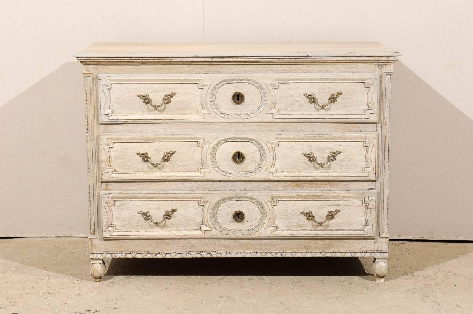 A French late 18th century three-drawer chest. This French chest features three drawers decorated with geometrical motifs and Rococo style hardware, as well as nicely carved molding. It is of a light cream color with a slight traces of yellow and is