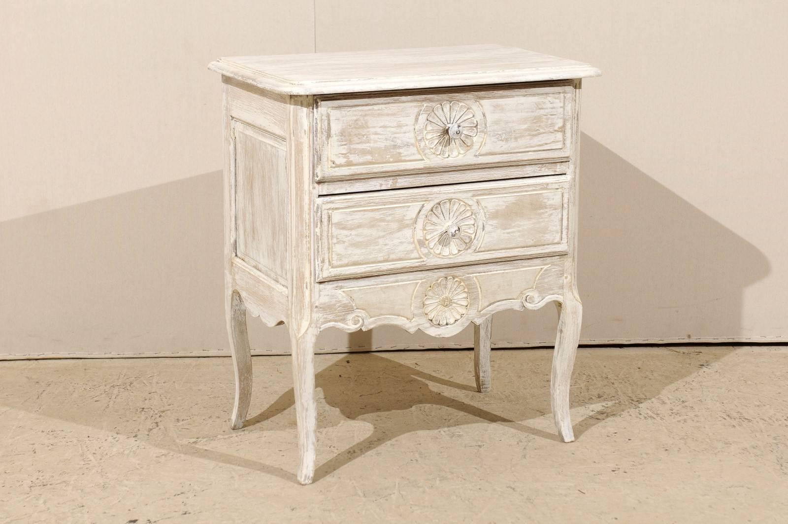 A small French 19th century two-drawer chest with a light white washed finish with some wood coming through. This French chest is decorated with three floral motifs on the drawers and the nicely carved skirt. It sits on four cabriole legs, circa