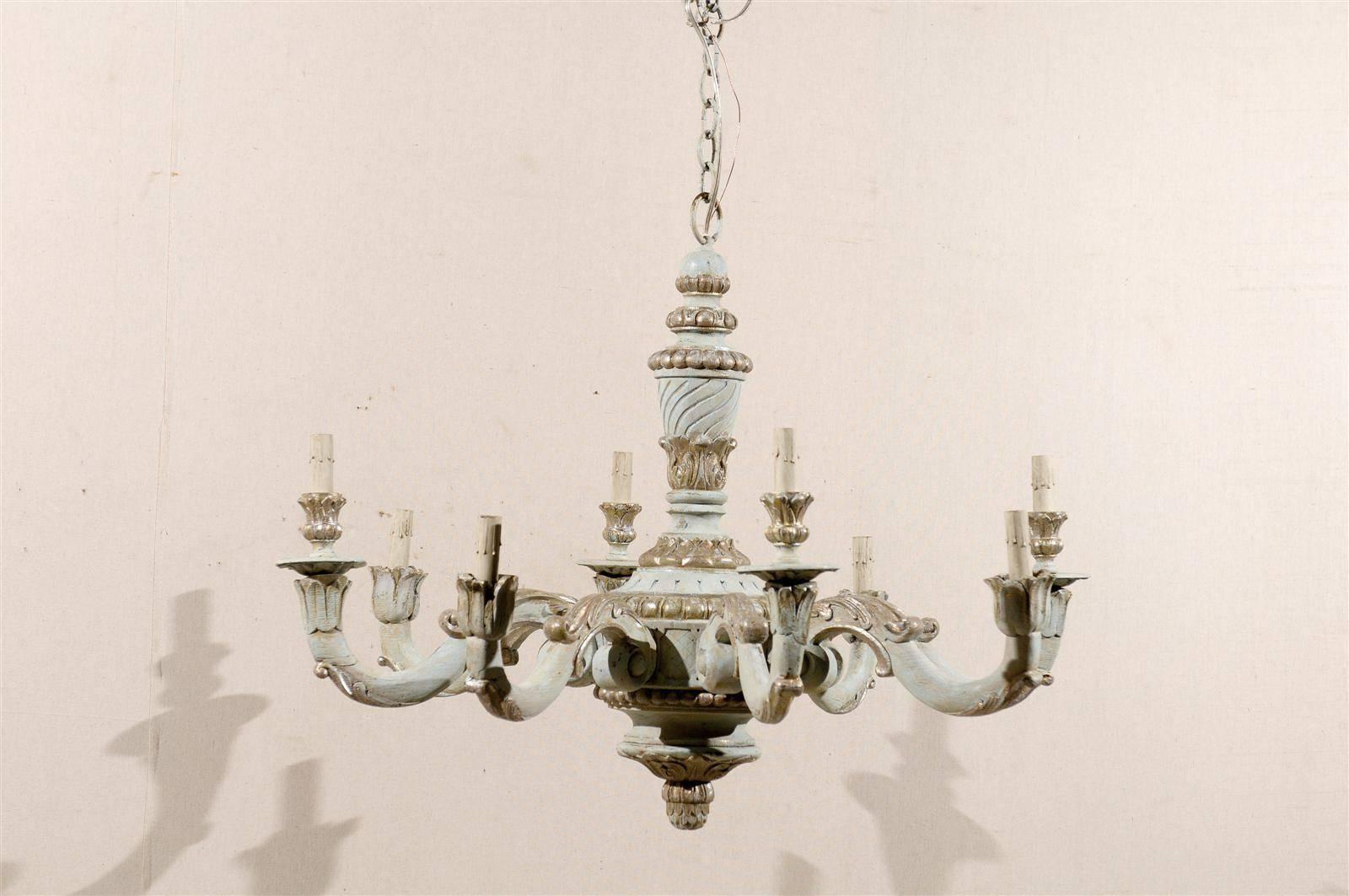 A French richly carved and painted eight-light wooden chandelier of light blue color with silver and slight green accents, nicely carved central column with various motifs such as egg-and-dart, scroll arms with acanthus leaves and delicate flower