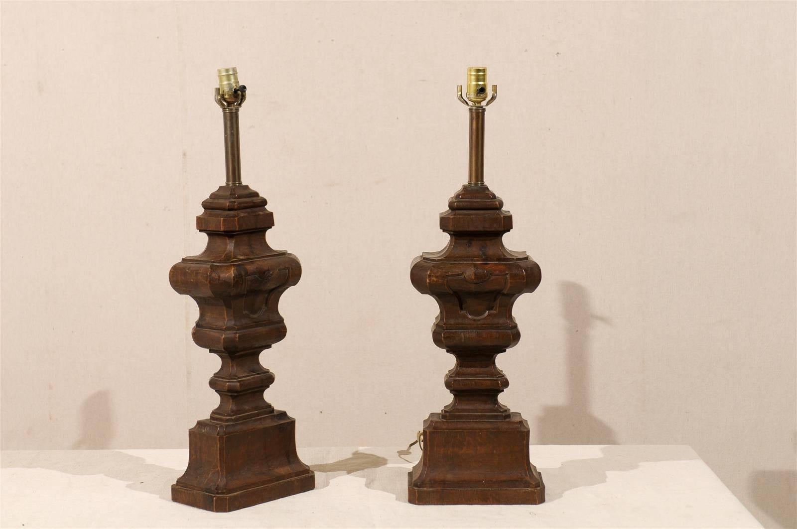 A pair of Italian carved wood table lamps. This pair of Italian wooden table lamps from the 20th century feature a brown color with more of a walnut color. This pair of Italian lamps has been rewired for the US. The wire comes out through the back.