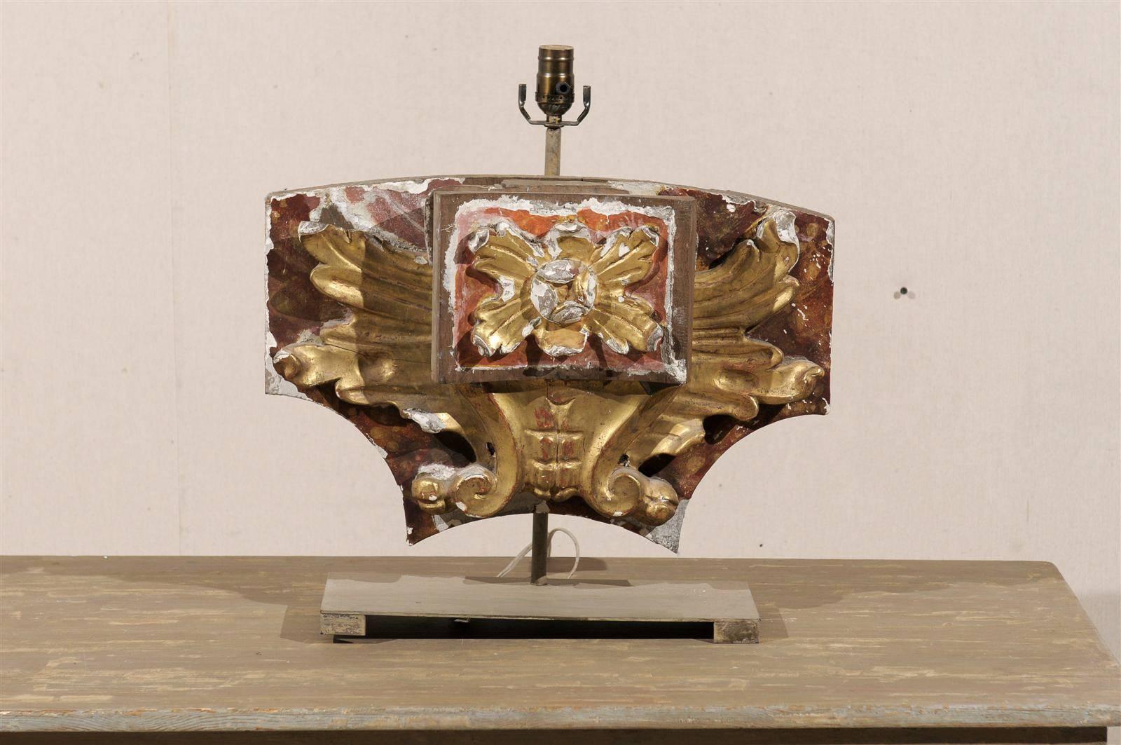 An Italian fragment made into a single table lamp from the early 20th century. This Italian fragment lamp features a central carved wood motif with giltwood flower on red painted background, over a second layer of gilded ornament. This fragment has