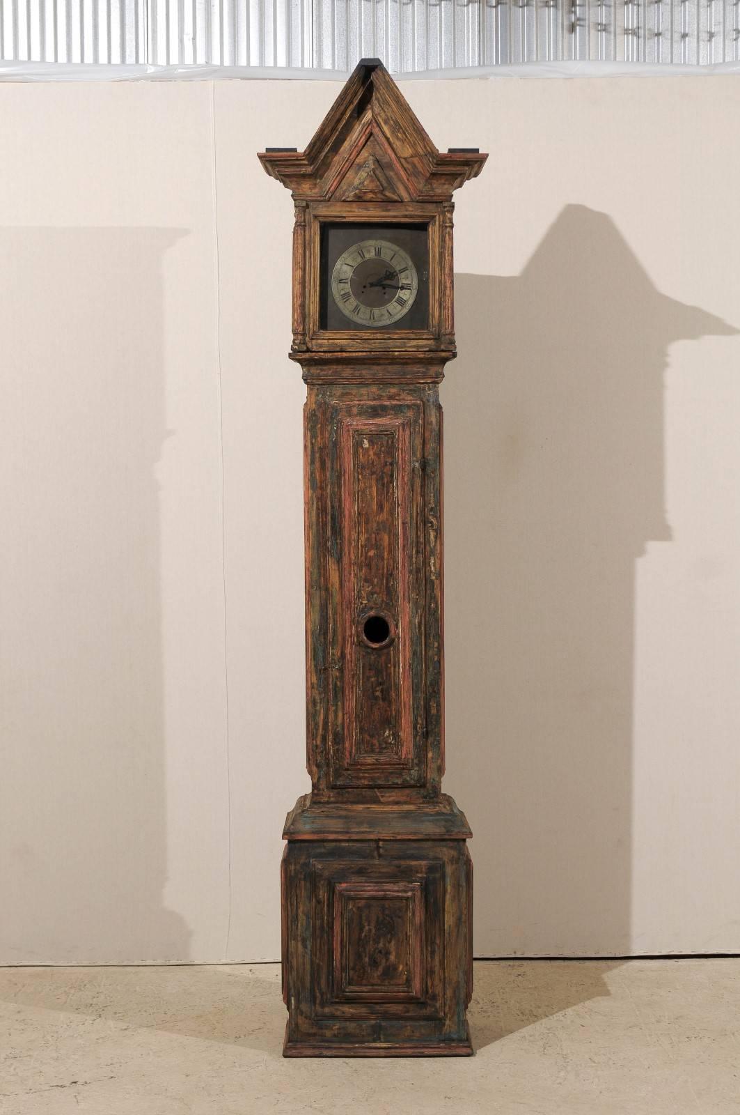Une horloge suédoise du 18ème siècle. Cette horloge suédoise en bois au profil linéaire présente une tête carrée surmontée d'une crête de forme triangulaire. Cette horloge a conservé sa face métallique, ses aiguilles et son mouvement d'origine.  Le