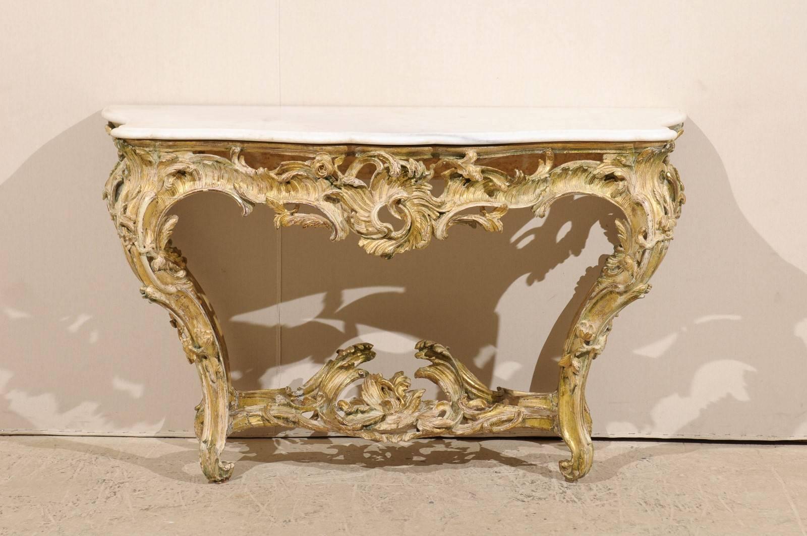 An exquisite French wood rocaille carved and gilt console table with marble top from the mid 18th century.  This period Rococo wall console table features the typical French rocaille vocabulary carved on the base, supporting the white marble top.
