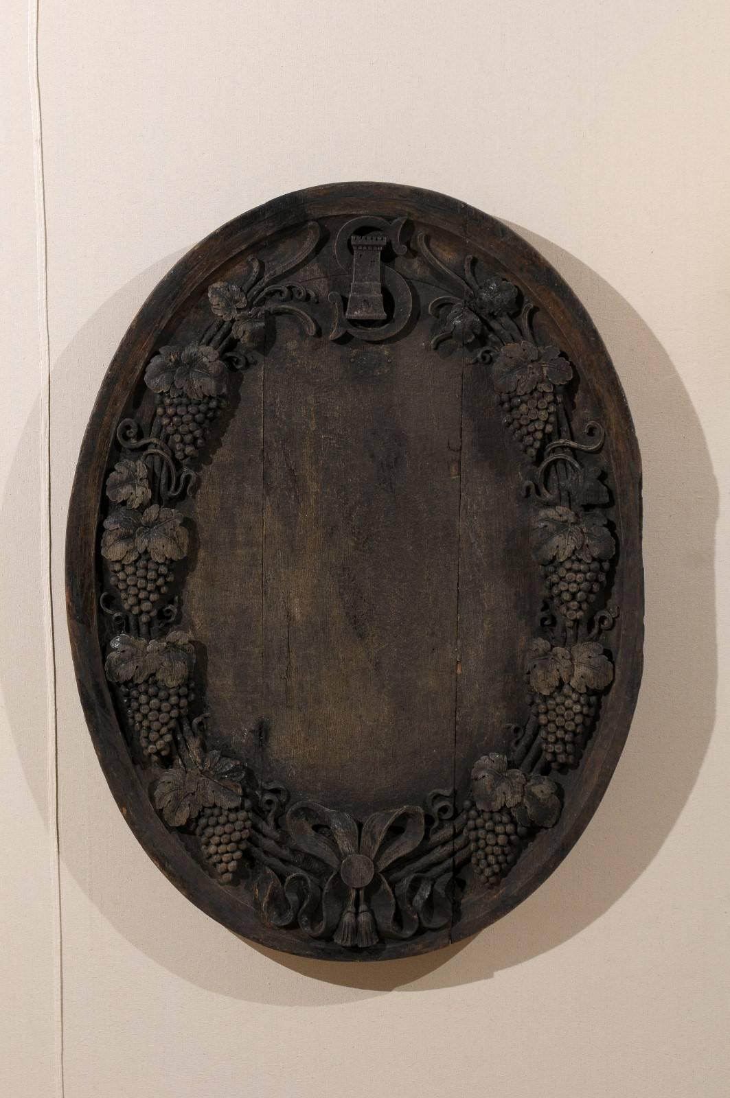 An elegant large French 19th century hand-carved wood wine cellar plaque. This lovely French wall hanging wine cellar plaque is oval shaped, made of dark wood and features motifs of intricate hand-carved grapes, ribbons and a medieval looking tower