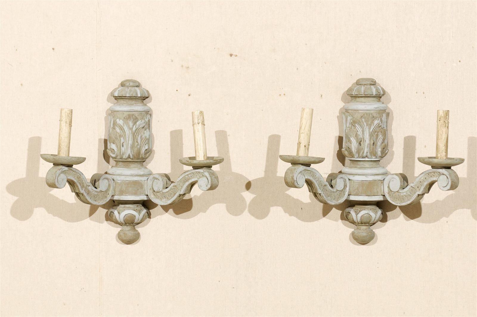 A pair of French carved and painted wood sconces. These scones are two-toned in color. The have carved acanthus leaf motifs on the central column. Two s-scroll arms on each sconce lead outward. Each sconce has a round finial at the bottom. These
